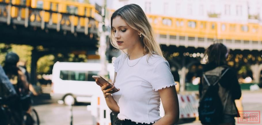 Young-woman-using-mobile-phone-while-walking-by-street-in-city.jpeg